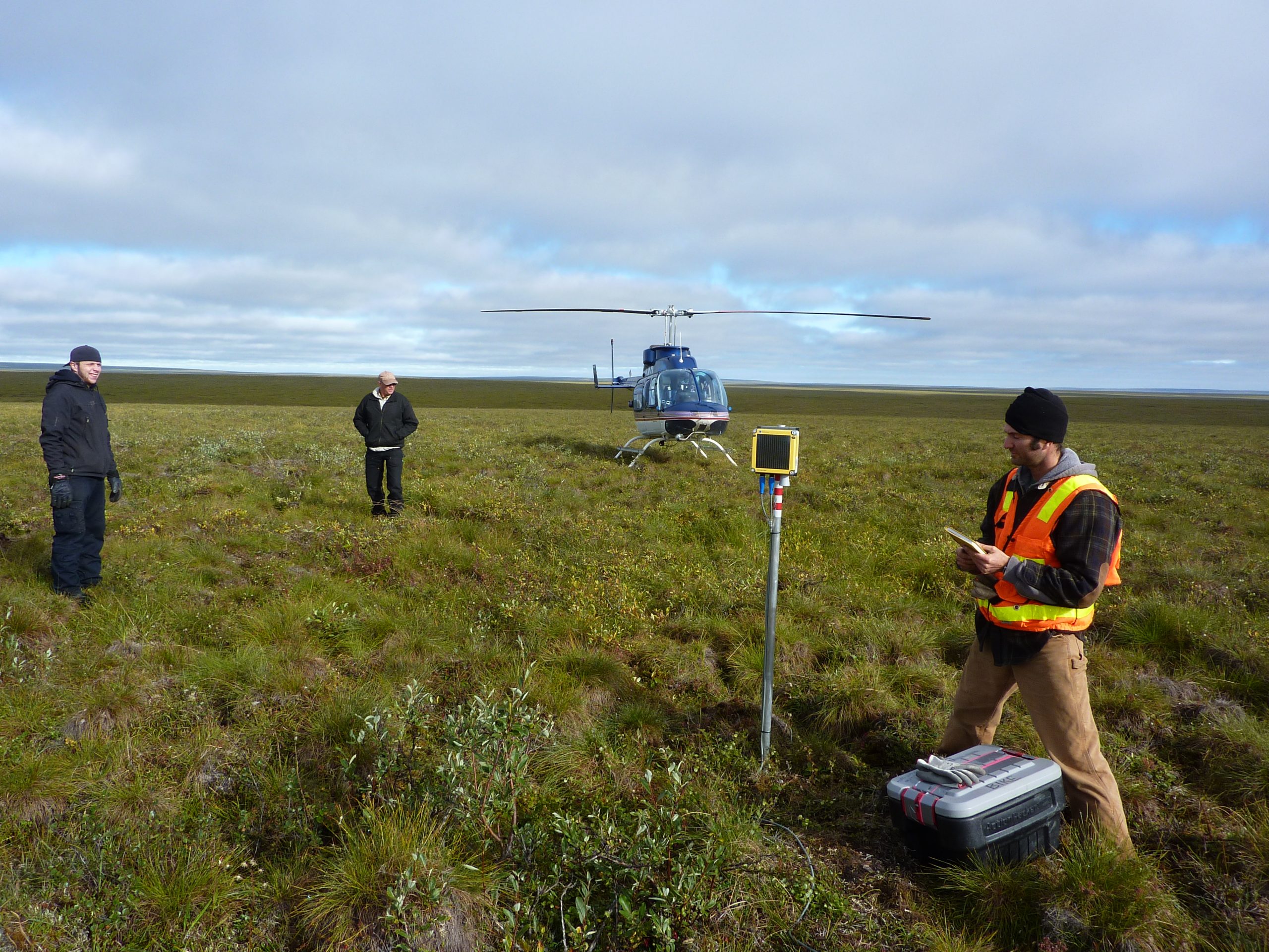 Beadedstream team installing thermistor strings and data logger in the Arctic tundra, helicopter in the background