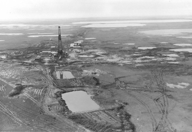 Aerial photo from 1968 of an exploration drill rig at Prudhoe Bay surrounded by vehicle tracks cut into unfrozen tundra